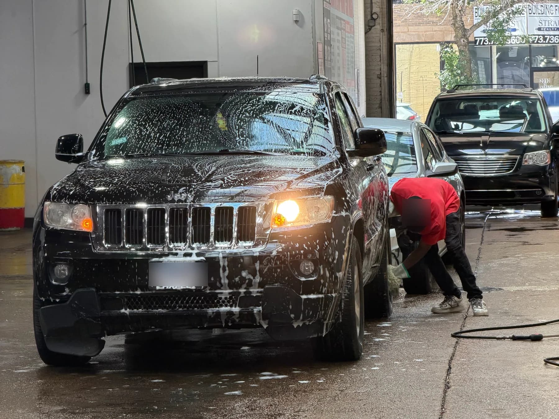 An SUV covered in foam while a team member scrubs its wheel by hand